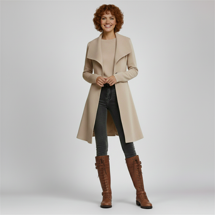 Woman wearing a beige coat, black pants, and brown boots on a light gray background