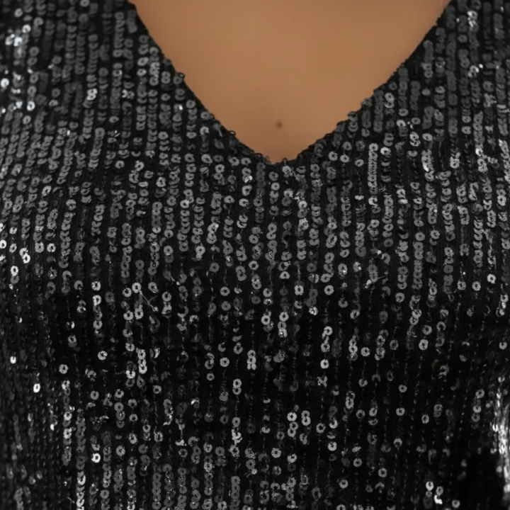 Woman sitting indoors wearing a black sequin V-neck sleeveless top paired with jeans in natural window light.