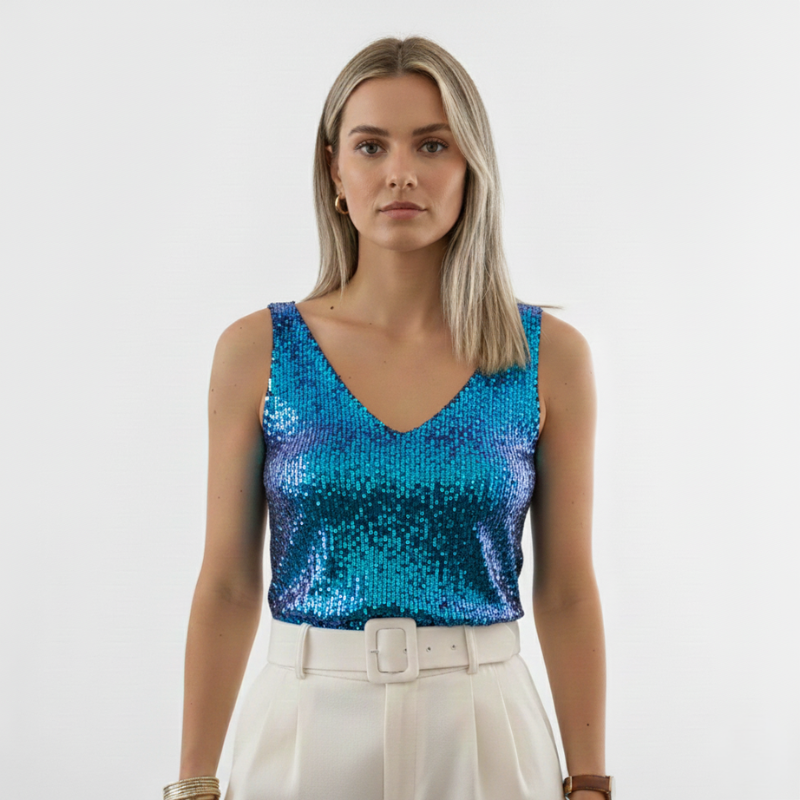 Full-body photo of a woman wearing a blue sequin top styled with white pants in bright studio lighting.