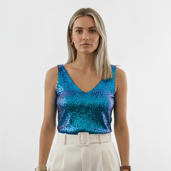 Full-body photo of a woman wearing a blue sequin top styled with white pants in bright studio lighting.