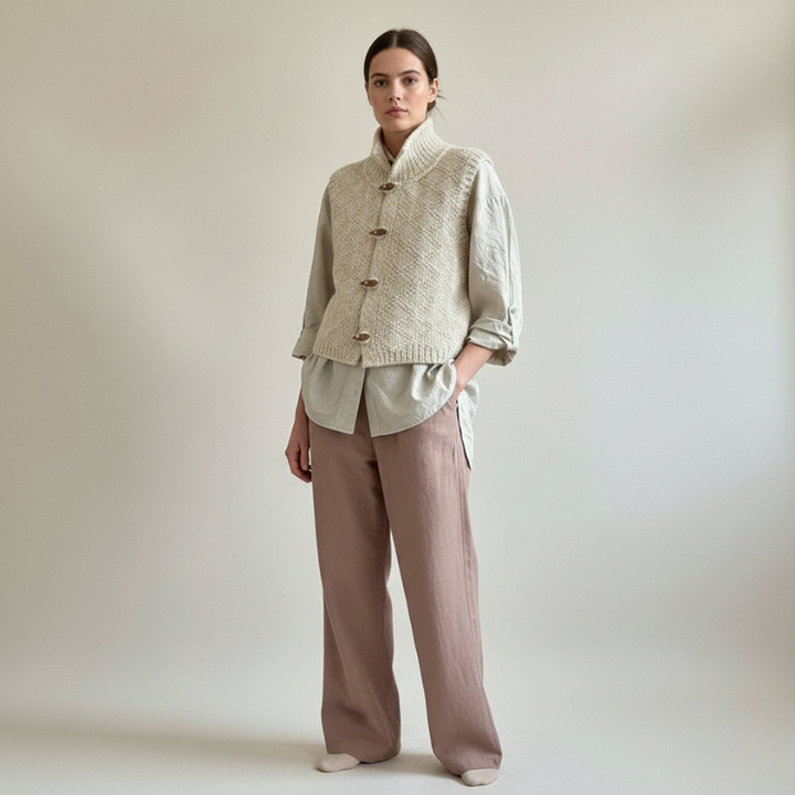 Woman wearing a beige knitted top and brown pants against a plain background