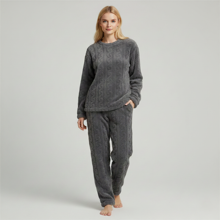 Woman wearing a dark gray fleece lounge set with a soft long-sleeve top and matching pants in a studio setting.