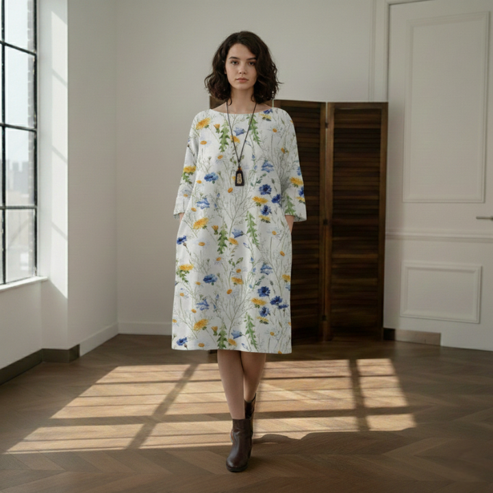 Woman wearing a white floral midi dress with blue and yellow prints in natural window lighting.