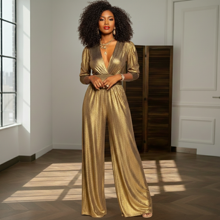Woman indoors wearing a gold satin evening jumpsuit with structured shoulders and wide-leg silhouette.