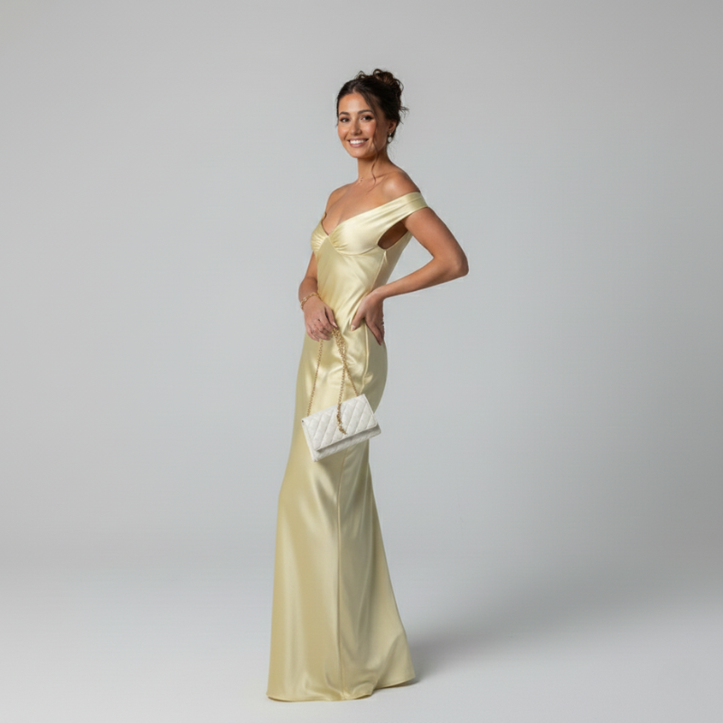 Woman in a light yellow evening gown holding a white clutch against a gray background