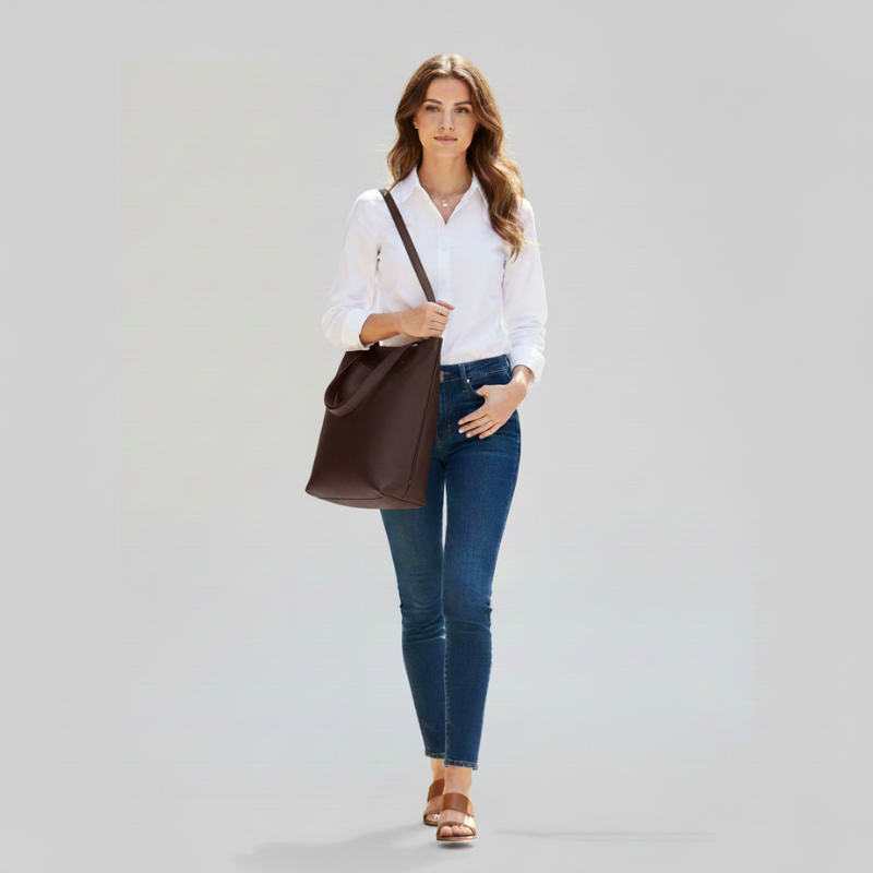 Female model walking with a brown leather tote bag styled casually with jeans and a white shirt.