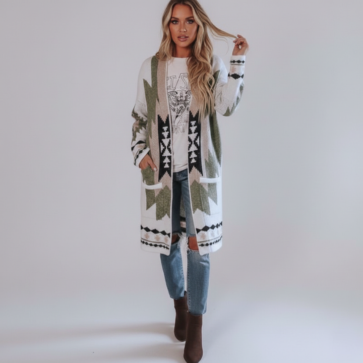 Woman wearing a long tribal-pattern knit cardigan in cream and green tones paired with jeans and boots in studio lighting.