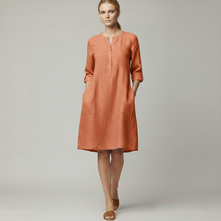 Woman wearing an orange knee-length casual dress with 3/4 sleeves and a minimal buttoned neckline in natural indoor lighting.