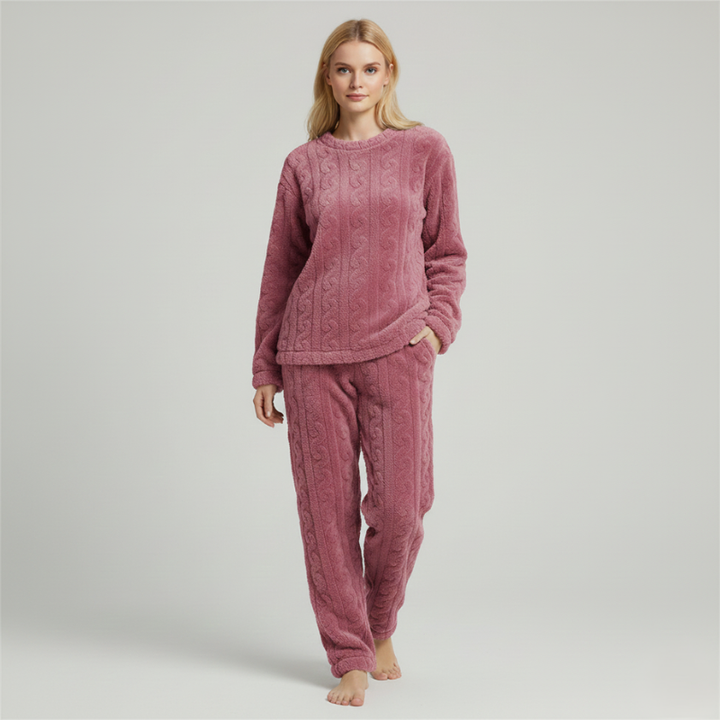 Woman wearing a pink fleece lounge set with a warm textured top and matching pants in soft studio lighting.