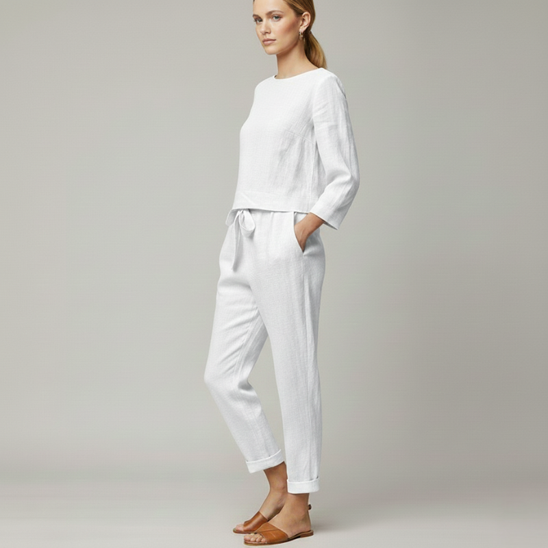 Woman wearing a white two-piece lounge outfit with a loose top and fitted jogger pants in soft studio lighting.