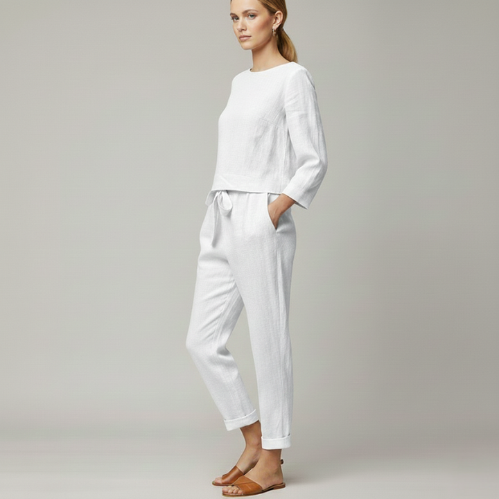 Woman wearing a white two-piece lounge outfit with a loose top and fitted jogger pants in soft studio lighting.