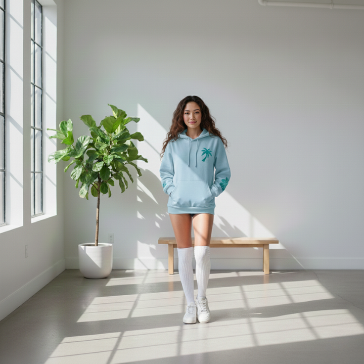 Woman in a light blue hoodie standing in a bright room with a plant and bench.