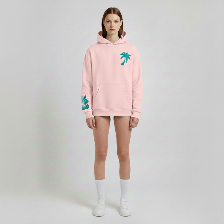 Person wearing a pink hoodie with palm tree designs on a plain background